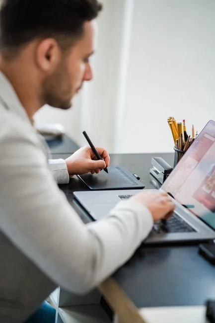 An outline of a fashion designer studying an inspirational mood board covered with fashion drawings and images.